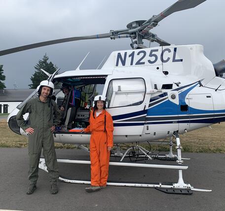 Color photo of two scientists standing in front of a helicopter. 