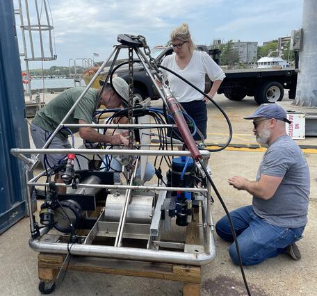 Three people working on a big instrument on a dock