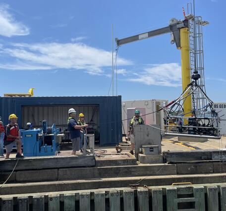 People on dock lowering large piece of equipment into the water