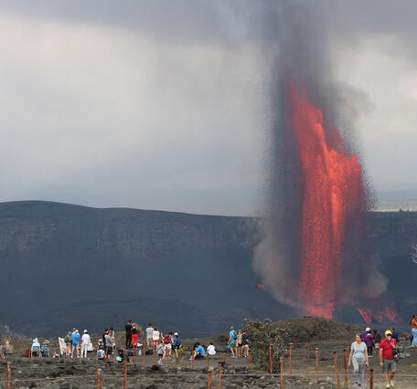 Lava fountains in the background with visitors visible in the foreground