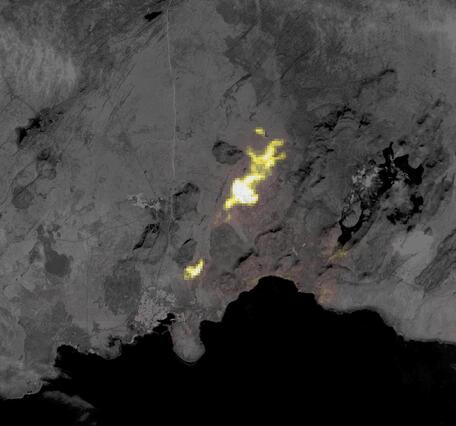 A thermal satellite image of an area of an erupting volcano that shines yellow to white on a gray landscape