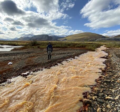 A person standing behind a pale orange river.