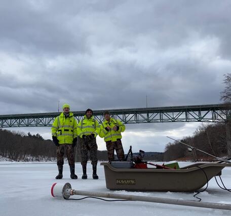 Three Scientists Standing on the Delaware River with their Ice Measurement Equipment in front of them