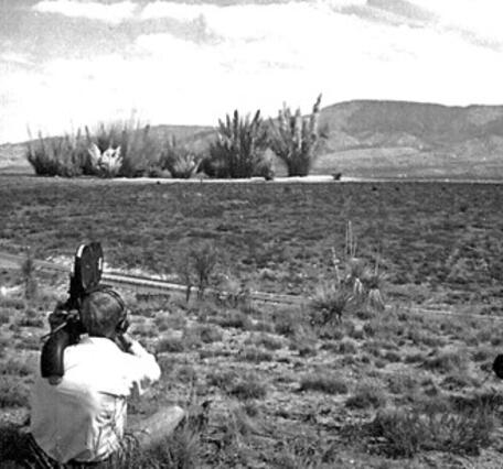 A cameraman (foreground) films small explosions in the distance, which are part of the creation of a crater field