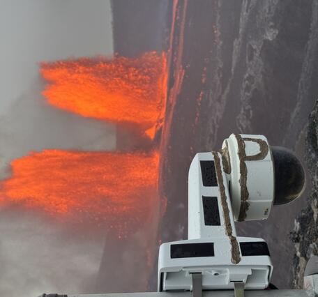 Color photograph of webcam in the foreground and lava fountains in the background
