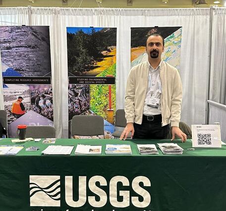 Dr. Iman Salehi Hikouei stands in front of the USGS booth at a conference.