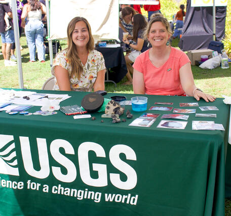 Two women sit at a USGS booth table at an outdoor event. 