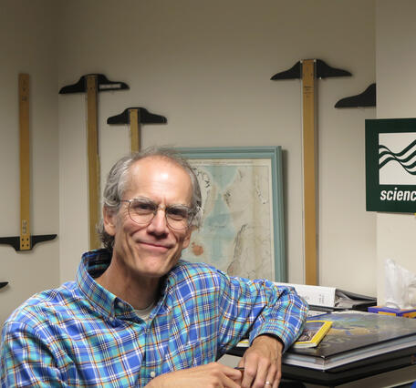 Jeremy Havens standing in front of the office T-square collection, which hang from the wall