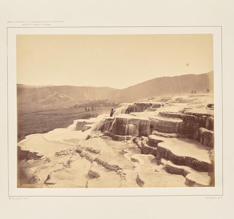 Sepia-toned photo of a man standing on a barren terraced hot spring formation