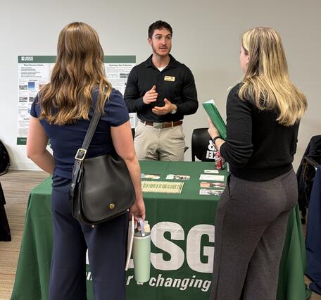 Man standing behind USGS table speaking to two women at a career fair