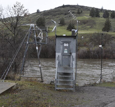 narrow rectangular metal gage house next to the river on a cloudy day.