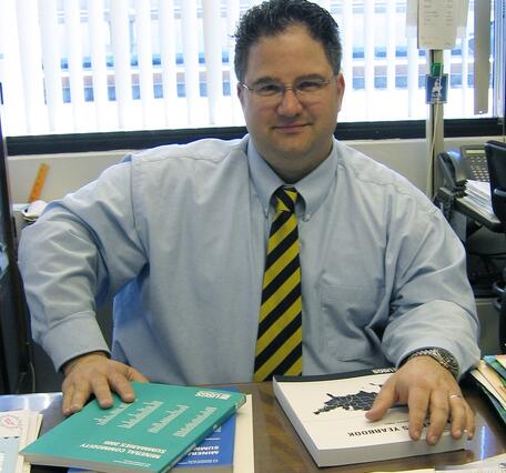 Jason Willett sits at a desk with books on geology on it.