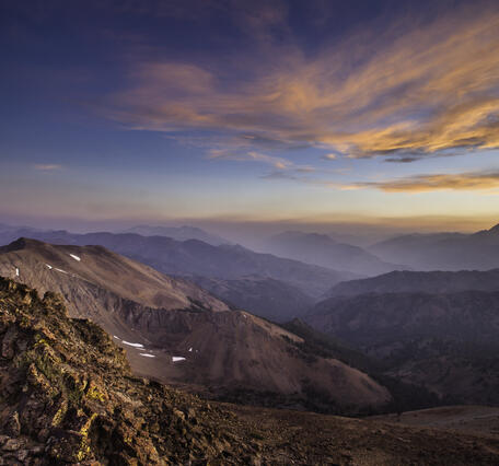 Barren and rocky mountainsides at sunset with some clouds in the distance