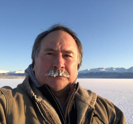 A man in a brown winter coat stands in a snowy landscape.