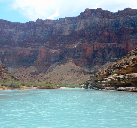 A red shade umbrella in the distance along the light blue Little Colorado River in Grand Canyon
