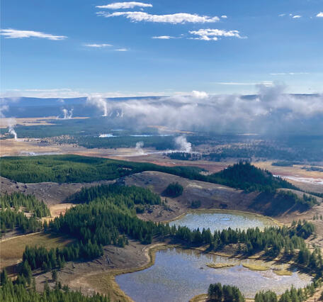 Small lakes occupy a landscape of forests and meadows under partly cloudy sky