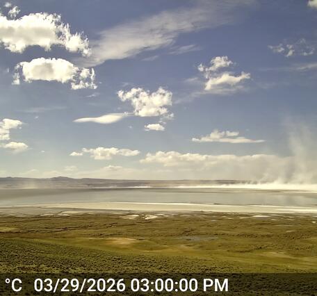 White dust blows off of shallow lake surface on a mostly sunny day