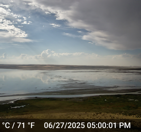 shallow lake water reflects a partly cloudy sky in the yellow landscape of the Oregon outback.