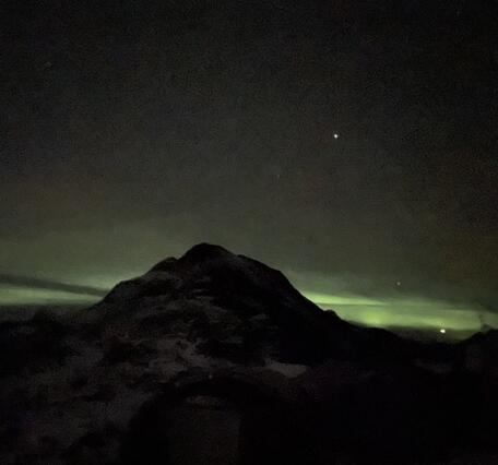 Dark mountain with green aurora behind.
