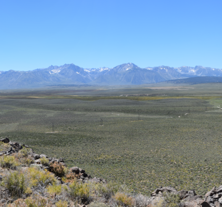View of a huge valley and distant mountain range. The valley is covered with sagebrush and rock outcrops