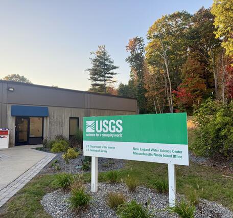 USGS Massachusetts office with a sign out front and trees in the back.