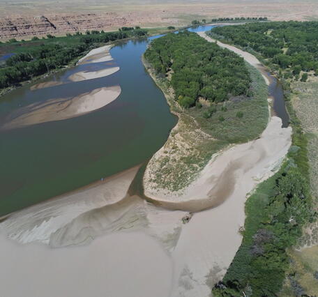 a blue-green river with many sand bars and beaches surrounded by trees and rock formations