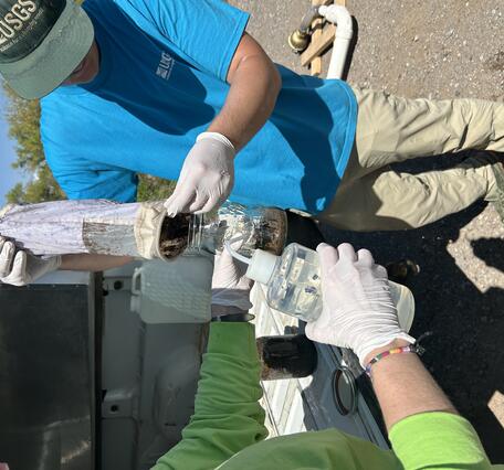 Two hydrologists transferring a collected microplastics sample into a jar. 
