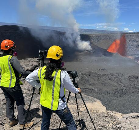 color photo of two geologist looking at the lava fountain in the background.
