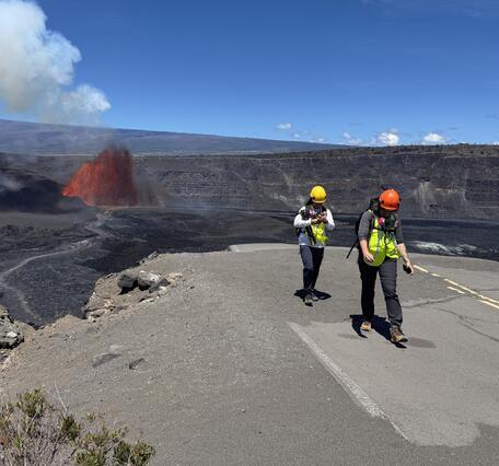 color photo of two scientists walking away after observing the lava fountain in the distance. 