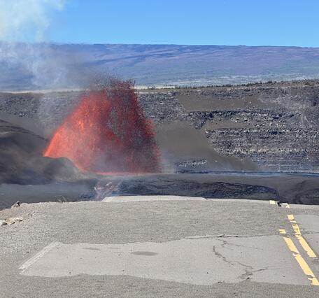 color photo of lava fountain visible beyond the end of a broken road.