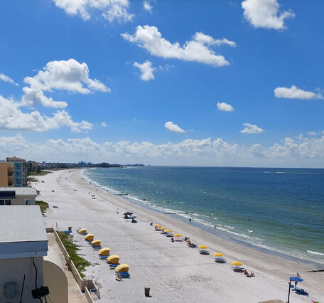 A view taken from a roof of a long white beach, yellow umbrellas on the beach, and a calm blue ocean in FL