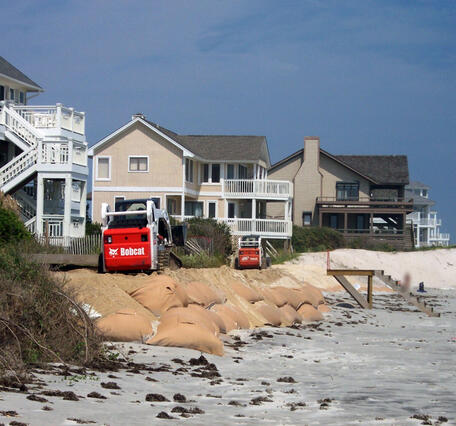 Make-shift seawall sandbags support an eroded dune below coastal homes on the beach