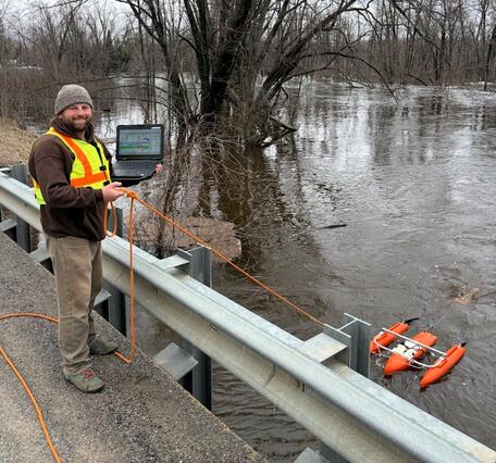 Hydrologic technician measures streamflow off bridge using ADCP on flooded river