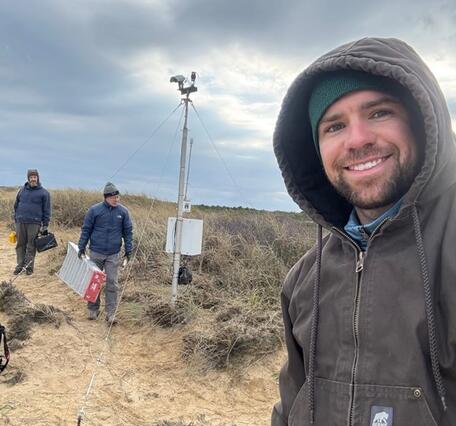 Three people on beach with camera mounted on tall pole