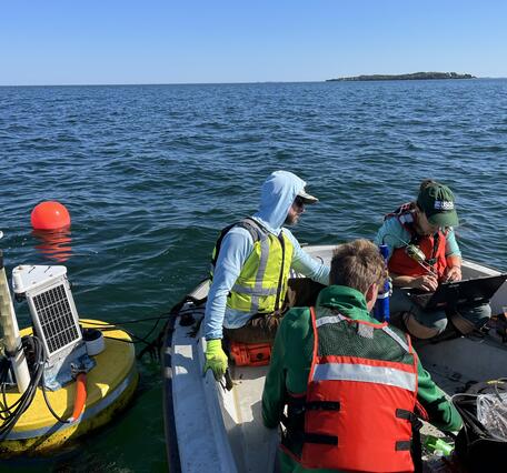 Three people sit in a boat surrounded by water and a buoy.