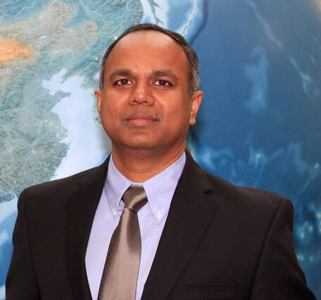 Md Shahriar Pervez staff photo. He is wearing a dark dress coat, a blue button shirt, silver tie and a map as a background.