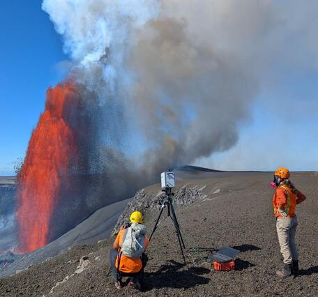 Color photograph of scientists measuring volcanic gas during eruption