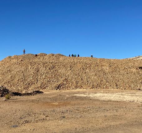 A pile of brown rocks, waste left after hard-rock mining, and behind it, blue sky.