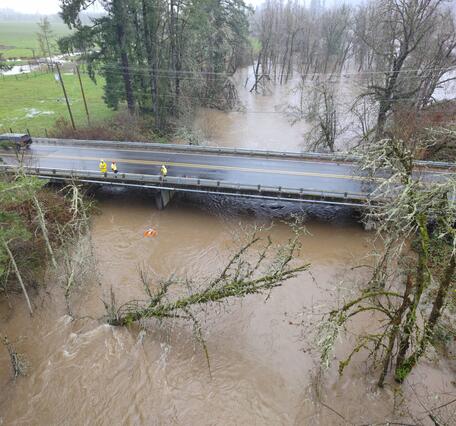 high up view, field crew are small brightly colored figures standing on a bridge while measuring