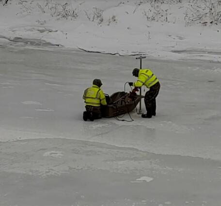 USGS Scientist standing on the frozen river lower equipment into the waters below through a hole in the ice