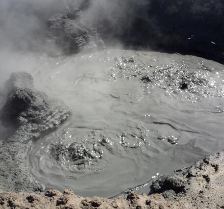 Boiling dark gray mud splashing within a small depression