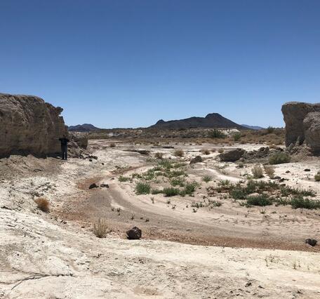 Dry desert landscape with rocky cliffs and sparse vegetation under a clear blue sky.
