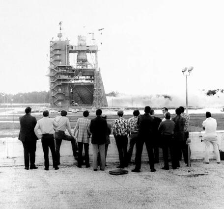 a group of men watch the first statis test-firing of the space shuttle main engine test in May 1975