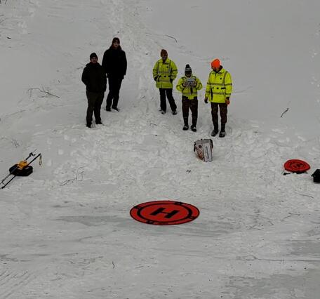 USGS scientists standing in the snow in front of an orange circular landing mat for their drone