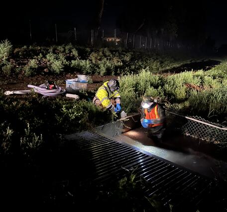 Two USGS employees sampling surface water in the dark during a rainstorm. 