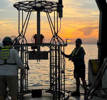 two people working with a mega multicorer on the deck of a ship at sunset