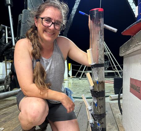 Person kneeling next to core sample on deck of ship at night