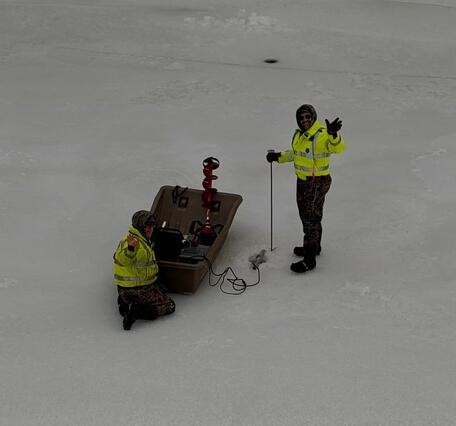 Two scientists next to an ice sled on the frozen Delaware River take a moment to wave at the camera