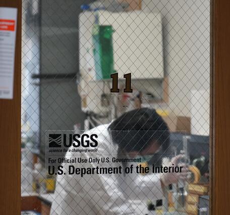 View of the lab from the outside, looking through glass window at scientist prepping samples