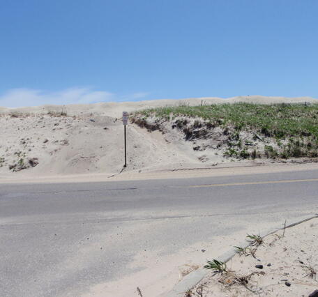 A dune that has sand washed over it next to a road during a storm